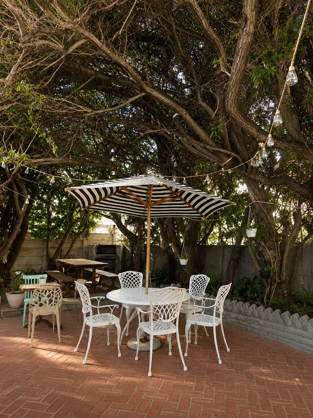 Shaded restaurant courtyard with outdoor tables, chairs and striped umbrella beneath large trees